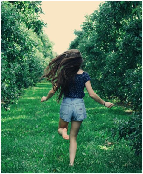 A girl joyfully runs through a sunlit orchard, enj