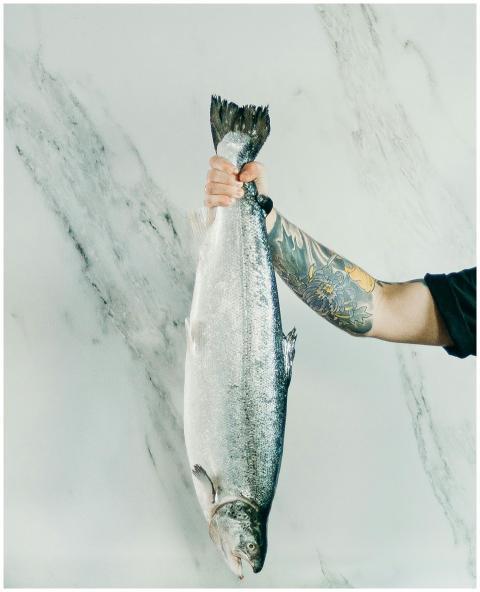 A tattooed arm holding a fresh fish against a marb
