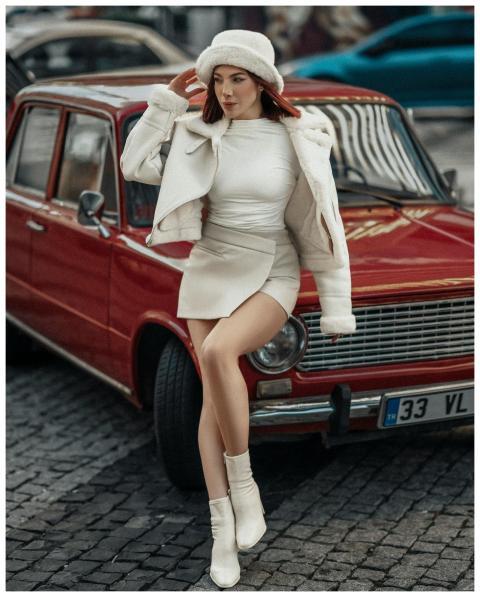 Stylish woman poses in white attire by a red vinta