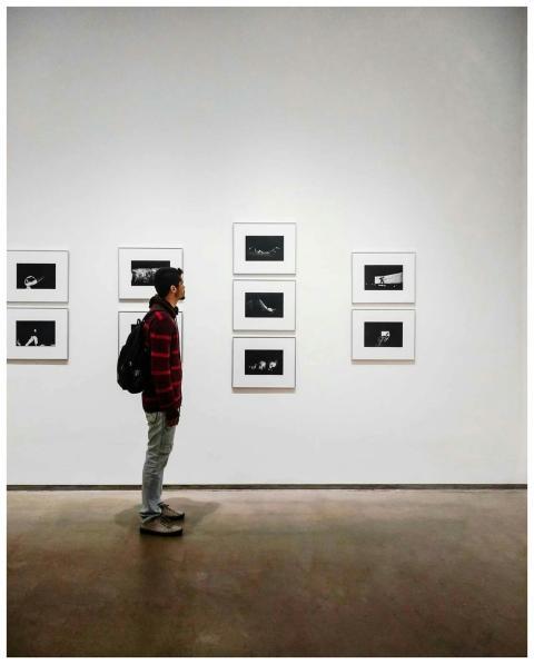A man stands in an art gallery, observing framed b