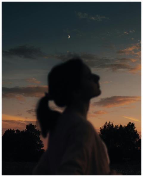 Silhouette of a woman at dusk under a crescent moo