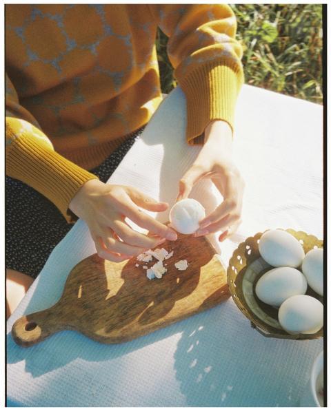 A person in a yellow sweater peels a hard-boiled e