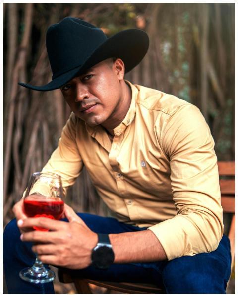 A man sits outdoors holding a glass of red wine wh