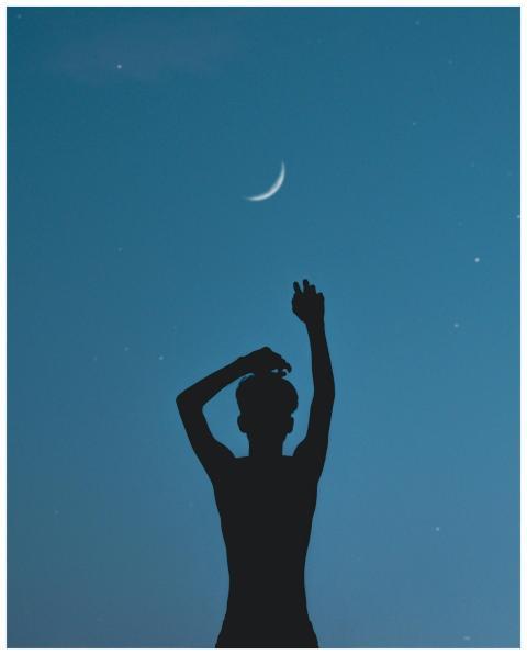 Silhouette of a person raising hands under the cre