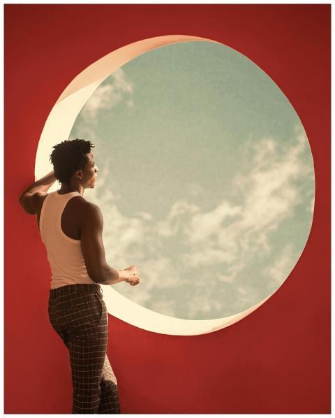 Man gazing through a circular window against a red