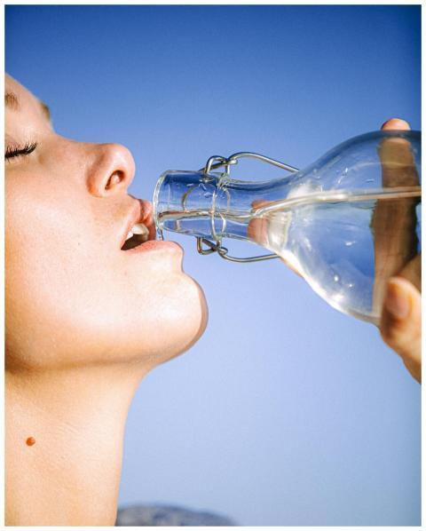 A woman drinking water from a glass bottle against
