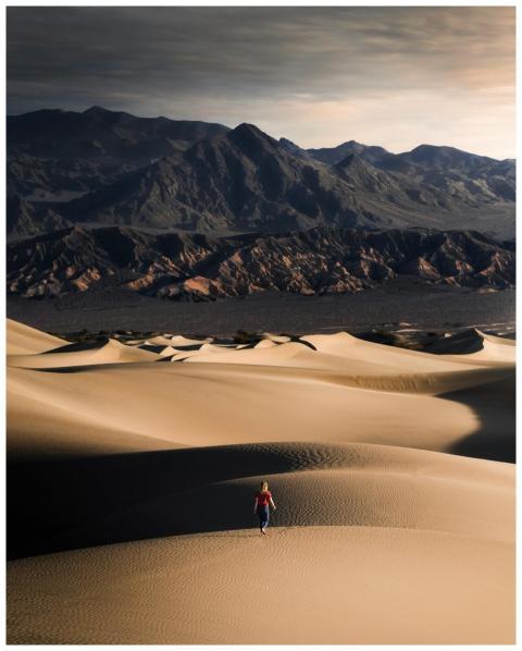 A woman walks alone across vast desert dunes with