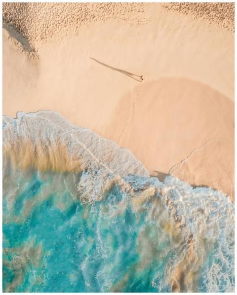 Drone view of anonymous person walking along sandy