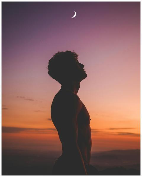 Silhouette of a man looking up at a crescent moon