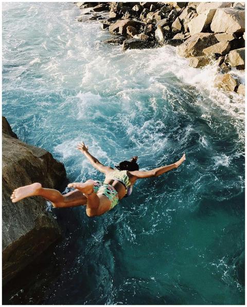 A woman in a bikini jumps off a cliff into the oce