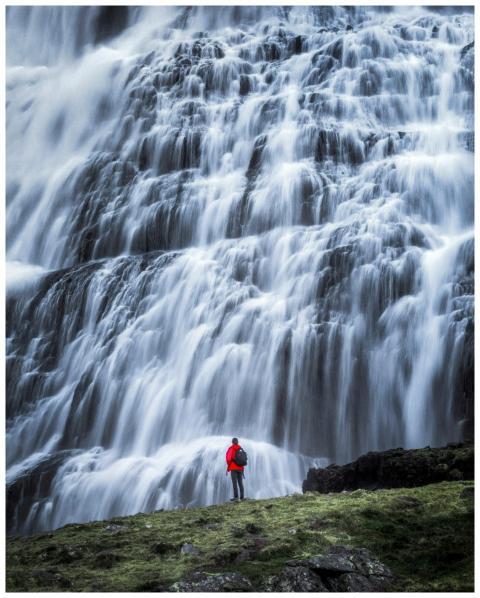 Hiker in red jacket stands before a grand waterfal