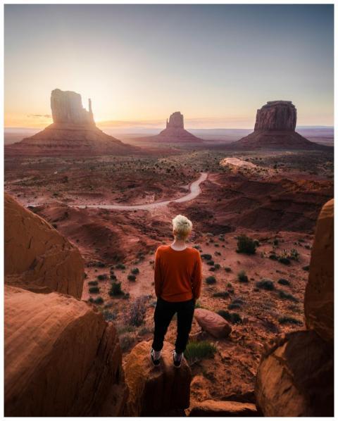 A person overlooks Monument Valley at sunrise, cap