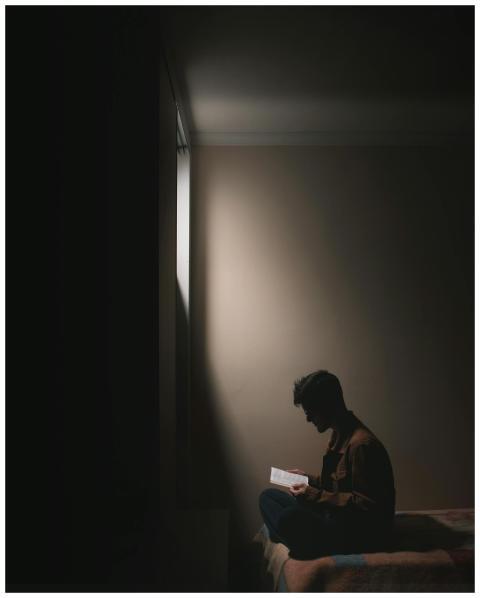 Silhouette of a man sitting on a bed in a dark roo
