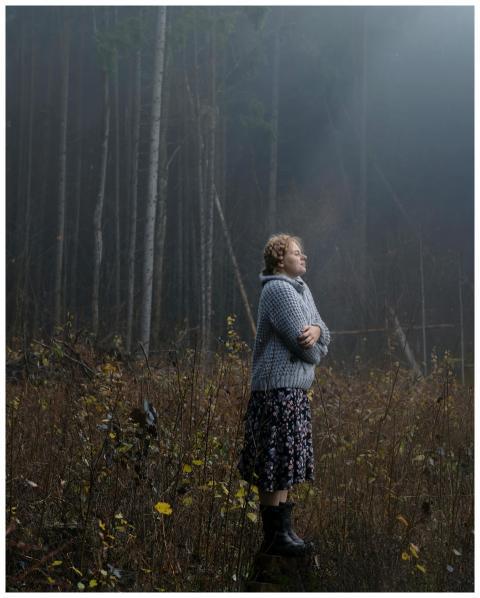 A woman stands in a misty forest, exuding a calm a