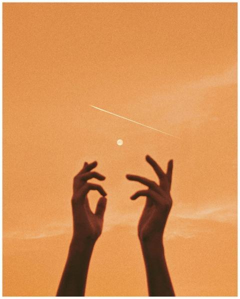 Silhouetted hands reaching up towards the moon and