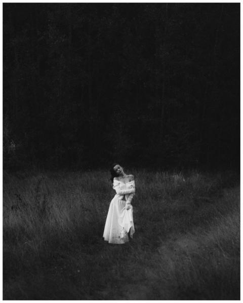 A woman in a flowing white dress stands in a dark,