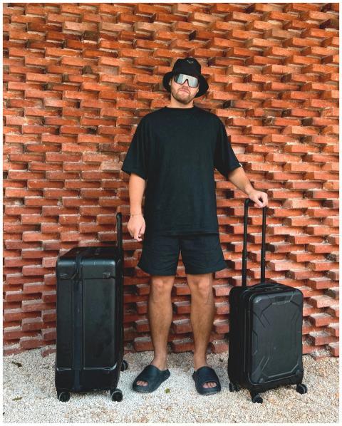 Man in black attire with suitcases stands against