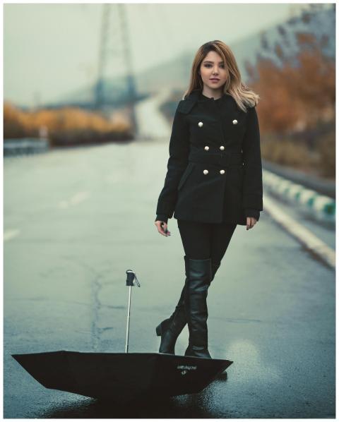 Stylish woman in black coat and boots stands with