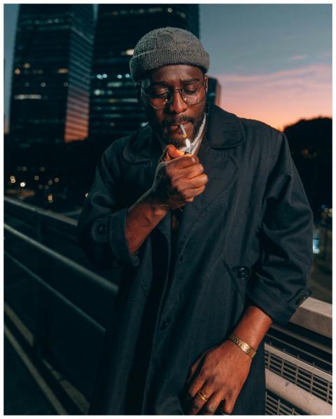 A man in a coat lights a cigarette on an urban bri