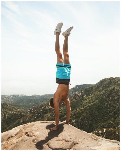 A fit man doing a handstand on a mountain peak wit