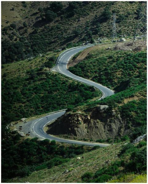 A winding road cuts through a lush green mountain