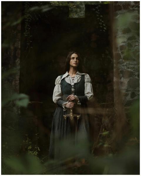 A woman in medieval clothing stands gracefully hol