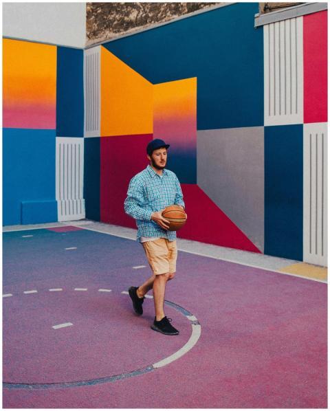 A man holding a basketball on a colorful, urban co