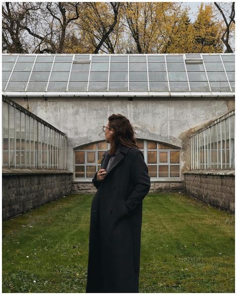 A person in a black coat stands outdoors near a gl