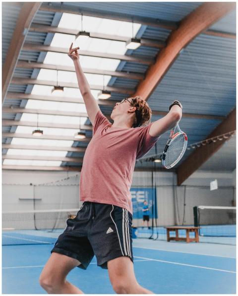 Tennis player serves energetically indoors, showca