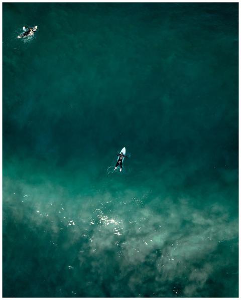 Aerial shot of surfers paddling on turquoise ocean