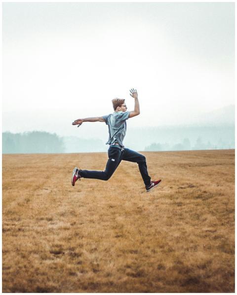 Man in motion leaps across a grassy autumn field,