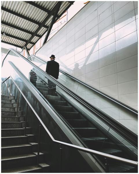 A man in a hat ascends an escalator in a modern su