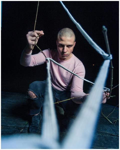 Bald man in ripped jeans and pink sweater poses wi