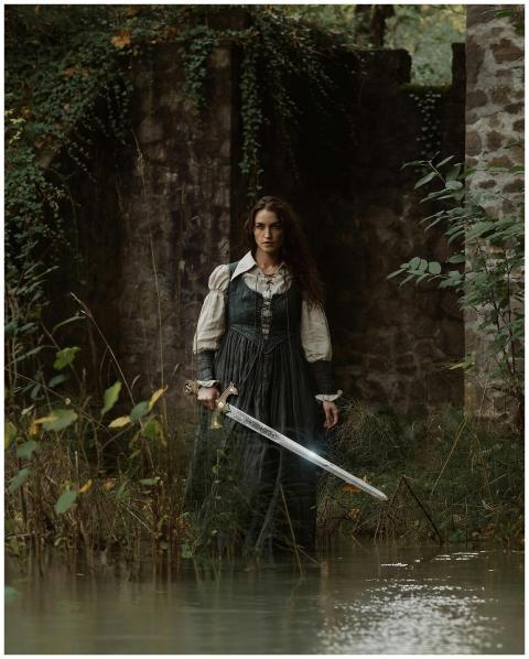 A woman in medieval attire holding a sword near a
