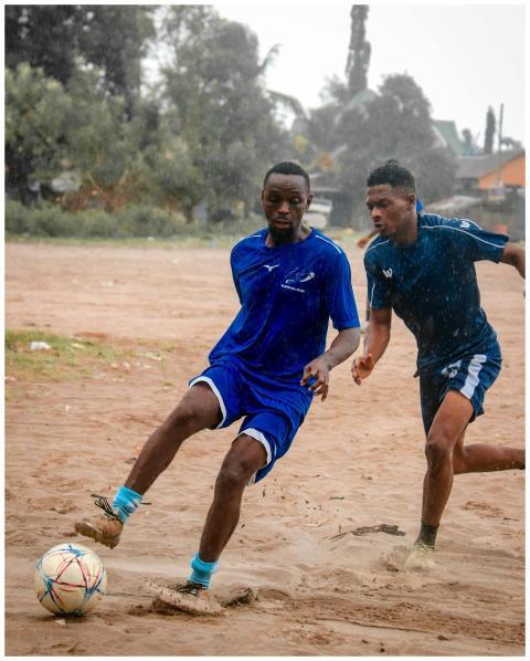 Two men playing soccer on a muddy field in Tanzani