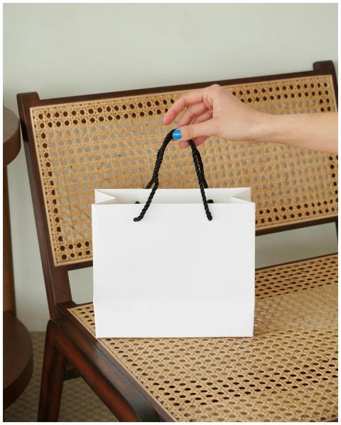 A hand reaches for a white paper bag placed on a w