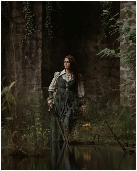 A woman in a medieval green dress standing by ston