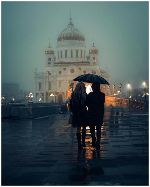 Couple under umbrella walks towards illuminated ca