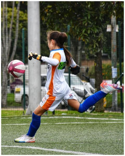 A young female soccer player actively kicking a ba