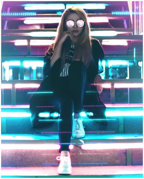 A fashionable woman sits on neon-lit stairs at nig