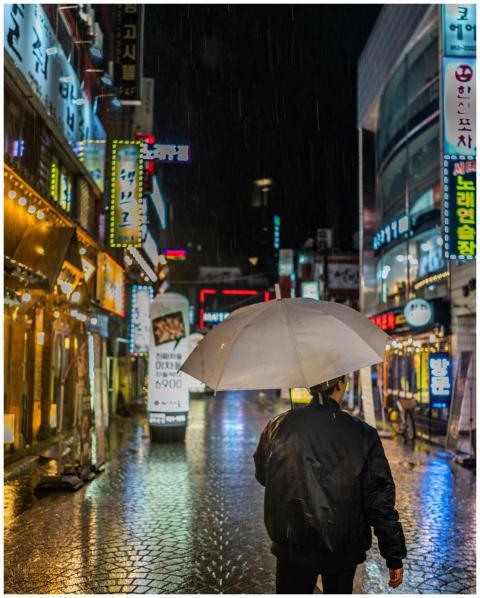 A person with umbrella walking through neon-lit st