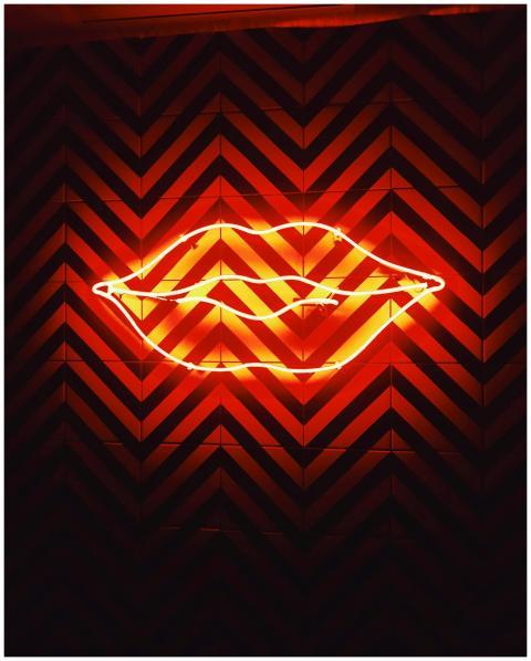 Vibrant neon lips sign glowing on a dark chevron p