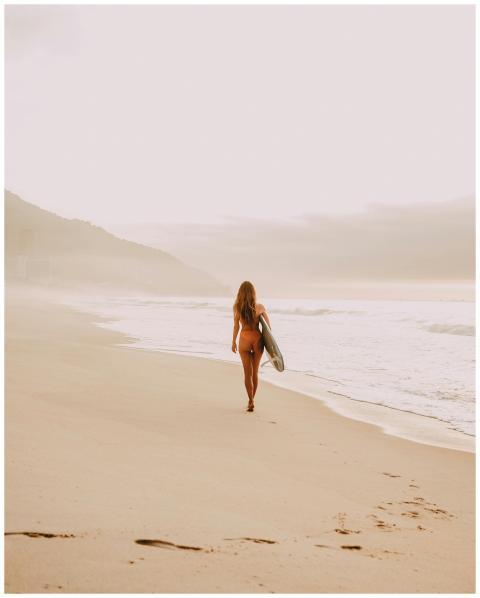 A female surfer walks along a serene beach in Rio