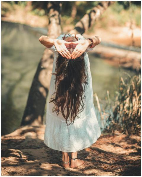 A woman with long hair performing a yoga pose by a