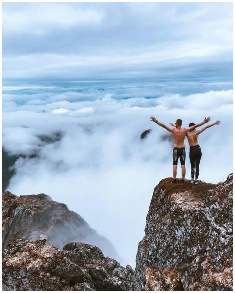 Two hikers stand on a rocky cliff, embracing the e