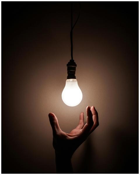A hand reaching towards a glowing hanging light bu