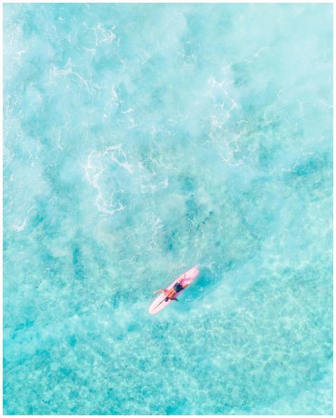 Aerial shot of a surfer paddling in vibrant blue w