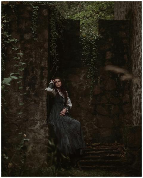 A woman in a green dress poses against an ivy-cove