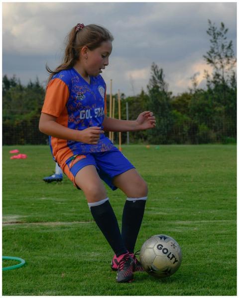 A young girl practicing soccer outdoors during the