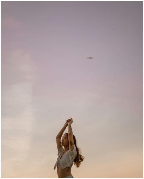 A woman with tattoos raises her arms against a col